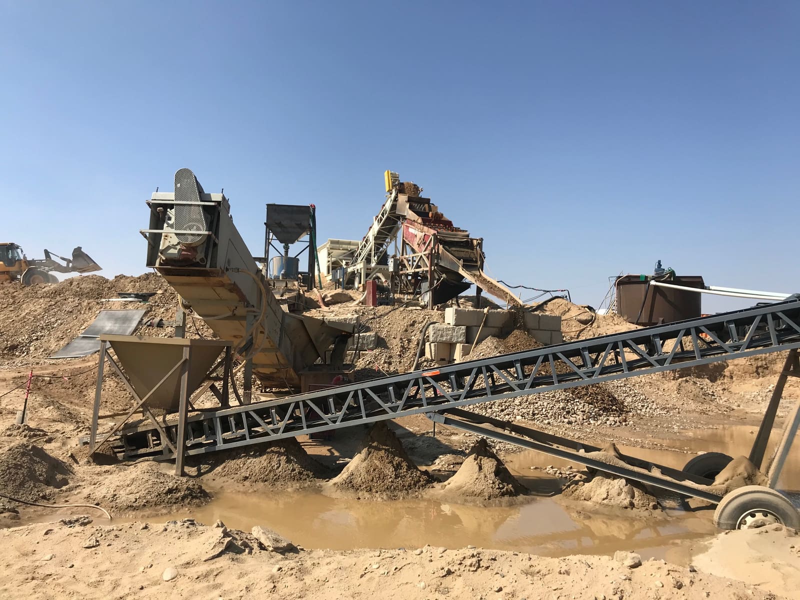 The wash plant working beside a muddy process pond, conveyors and sluices running.
